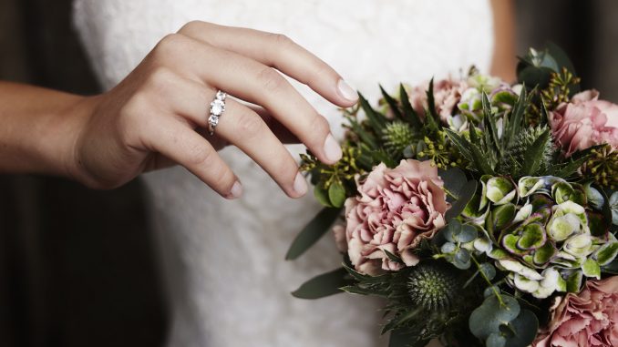 Bride wearing wedding ring near flowers